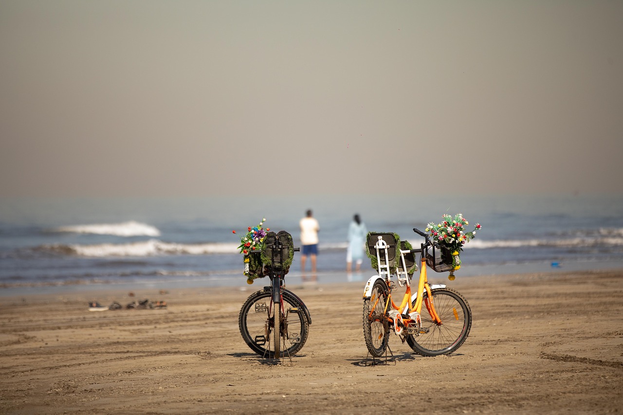 Two decorated bicycles parked on a Mumbai beach with people at the water’s edge